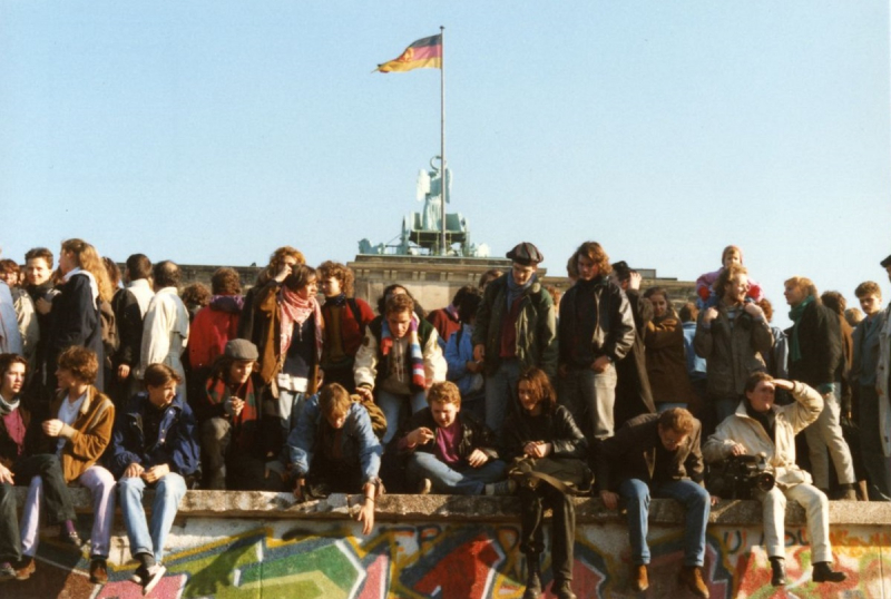 Menschen sitzen auf der Mauer vor dem Brandenburger Tor